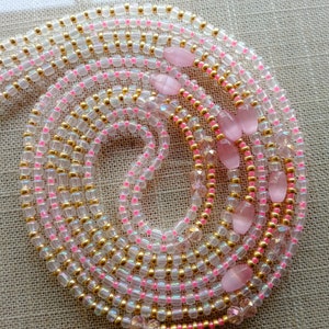 May include: A multi-strand beaded waist chain with pink and gold beads. The chain features several pink oval-shaped stones.