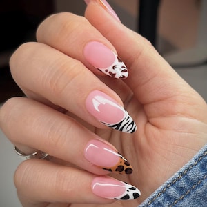 May include: A hand with long, almond-shaped nails. The nails feature a pink base with a white and animal print design on the tips. The animal prints include a cow print, leopard print, and zebra print.