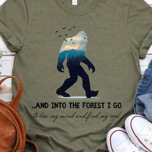 Peut inclure: Un t-shirt vert avec une silhouette de Bigfoot marchant dans une for&ecirc;t. Le texte sur le t-shirt est "...AND INTO THE FOREST I GO to lose my mind and find my soul".