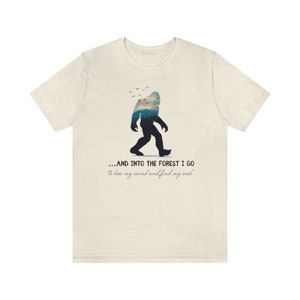 Peut inclure: Un t-shirt beige avec une silhouette de Bigfoot marchant dans une for&ecirc;t. Le texte dit "...AND INTO THE FOREST I GO to lose my mind and find my soul."