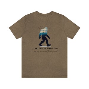 Peut inclure: Un t-shirt marron avec une silhouette de Bigfoot marchant dans une for&ecirc;t. Le texte sur le t-shirt est "...AND INTO THE FOREST I GO to lose my mind and find my soul."