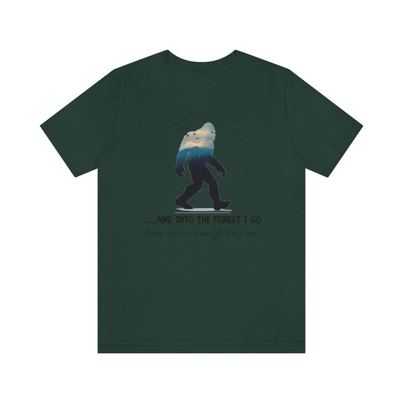 Peut inclure: Un t-shirt vert fonc&eacute; avec une silhouette de Bigfoot marchant dans une for&ecirc;t. Le texte sur le t-shirt est "...and into the forest I go to lose my mind and find my soul."
