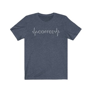 Pode incluir: Uma camiseta azul escura com um gr&aacute;fico de batimento card&iacute;aco branco e a palavra "COFFEE" dentro do batimento card&iacute;aco.