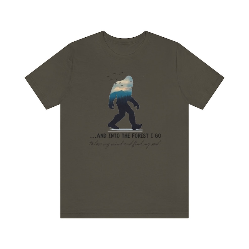 Peut inclure: Un t-shirt vert fonc&eacute; avec une silhouette de Bigfoot marchant dans une for&ecirc;t. Le texte sur le t-shirt est "...AND INTO THE FOREST I GO to lose my mind and find my soul."
