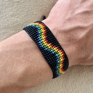 May include: A black beaded bracelet with a rainbow pattern. The bracelet is made of small, colorful beads and is tied with a black cord.