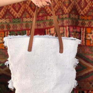 Pode incluir: Sacola tote branca com al&ccedil;as de couro marrom e detalhes em franjas. A sacola &eacute; feita de um tecido macio e texturizado.