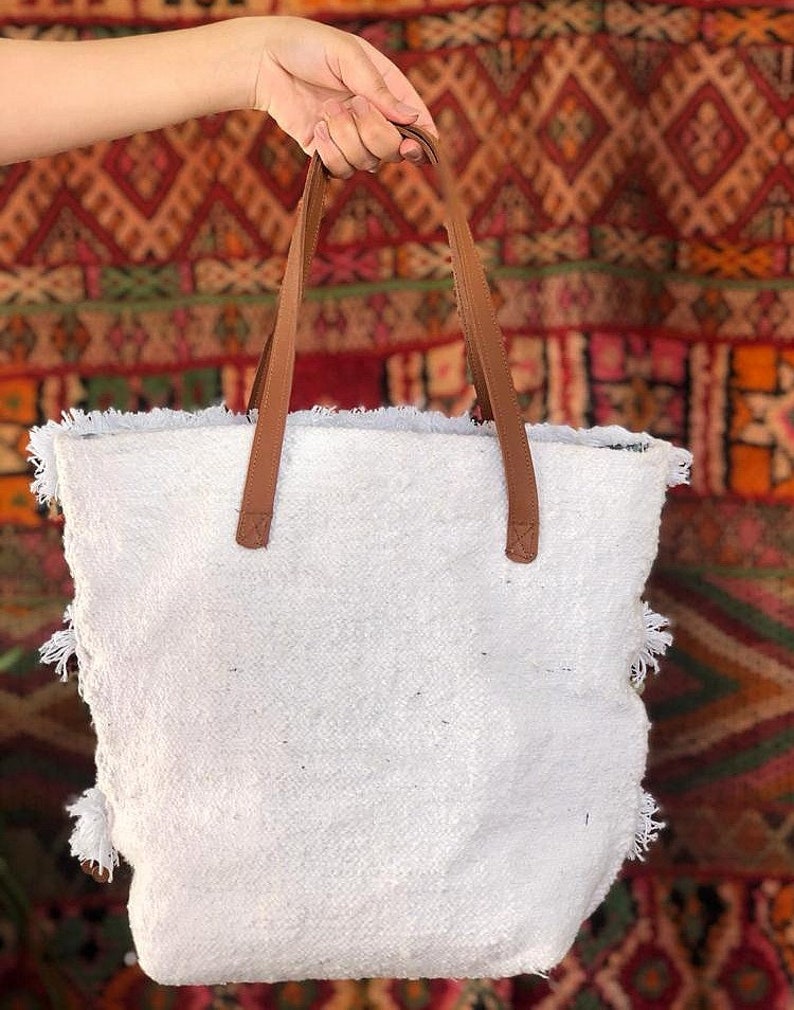 Pode incluir: Sacola tote branca com al&ccedil;as de couro marrom e detalhes em franjas. A sacola &eacute; feita de um tecido macio e texturizado.