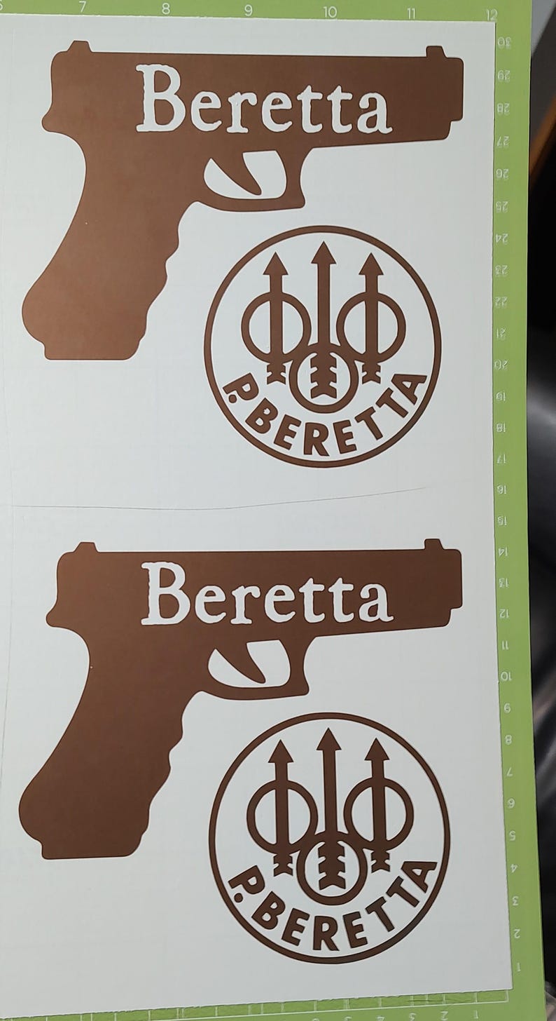 K&ouml;nnte beinhalten: Braune Vinylaufkleber mit dem Wort "Beretta" in Wei&szlig;, einer Pistouetten-Silhouette und einem kreisf&ouml;rmigen Logo. Das Logo enth&auml;lt das Wort "Beretta" und ein stilisiertes Design.