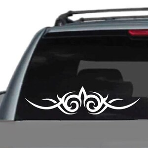 K&ouml;nnte beinhalten: Wei&szlig;es Tribal-Design-Autoaufkleber. Der Aufkleber hat ein symmetrisches Muster mit geschwungenen Linien und Wirbelelementen, geeignet f&uuml;r die Anbringung an der Heckscheibe oder Karosserie eines Fahrzeugs.