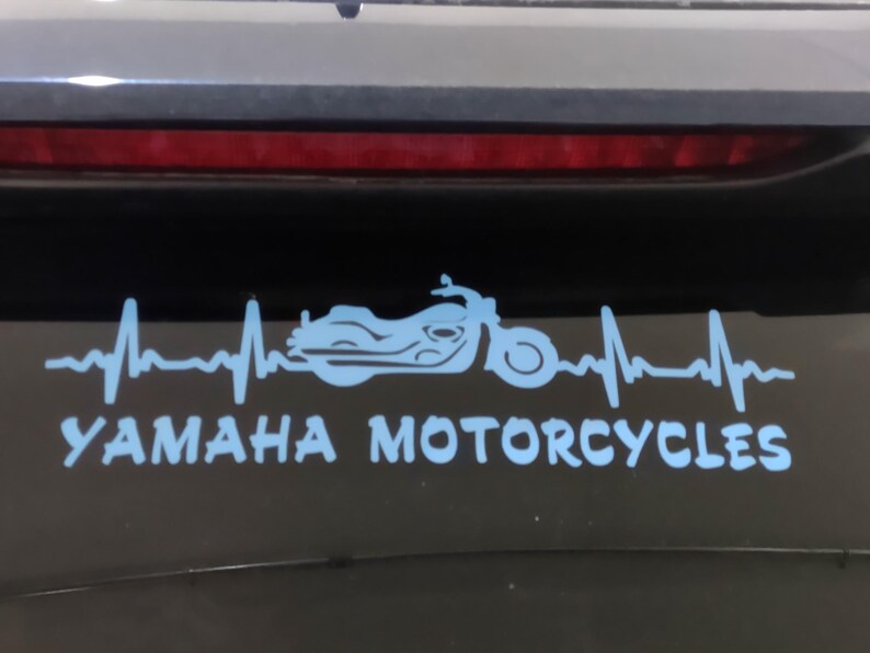 K&ouml;nnte beinhalten: Hellblauer Yamaha Motorcycles Aufkleber mit einer Motorradsilhouette in einer Herzschlaglinie. Der Text "YAMAHA MOTORCYCLES" befindet sich darunter. Der Aufkleber befindet sich auf einer dunklen Oberfl&auml;che.