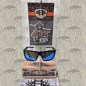 May include: Black sunglasses with blue mirrored lenses are displayed with packaging featuring a cowboy graphic and the text "SUMHOLLER AMERICA". The sunglasses have a rectangular frame and blue accents.