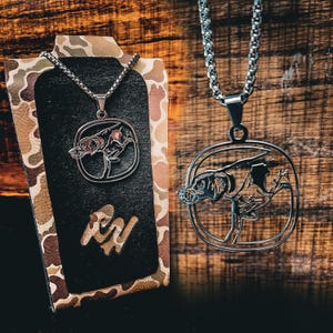 May include: Two silver necklaces with a dog silhouette pendant. The pendant on the left is a solid silhouette, while the pendant on the right is an outline silhouette.