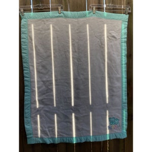 May include: A white baby blanket with a turquoise border. The blanket has a light blue and white striped pattern and says "Baby" in colorful letters.