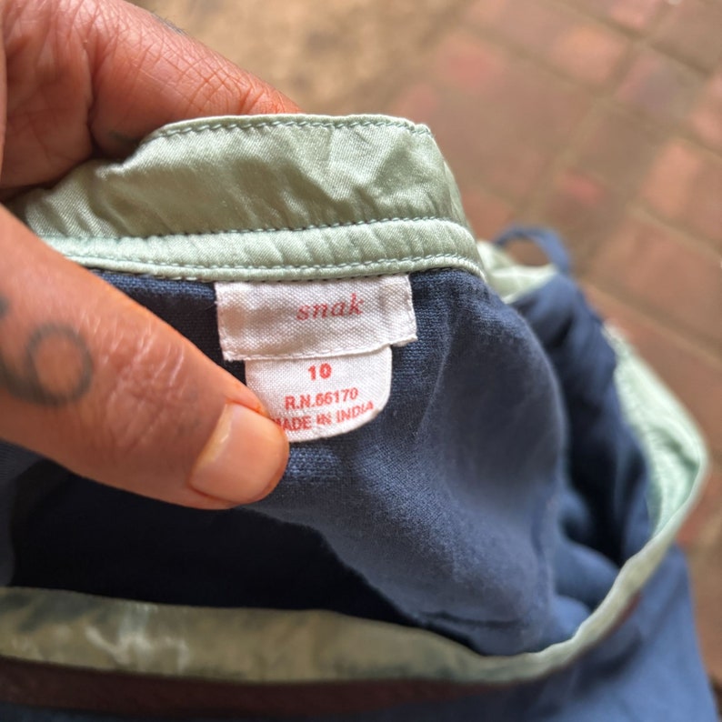 Puede incluir: Una etiqueta de ropa para ni&ntilde;os azul y verde con el texto "snak" y "10" impreso en ella. La etiqueta tambi&eacute;n incluye el texto "R.N. 66170" y "Hecho en India".