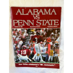 Peut inclure: Une couverture de programme de match de football vintage présentant le match Alabama contre Penn State le 25 octobre 1986 au stade Bryant-Denny à Tuscaloosa, en Alabama. La couverture est bordeaux avec du texte blanc et une photo de joueurs en action.