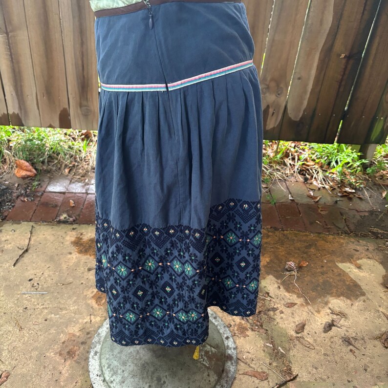 Puede incluir: Una falda azul con una cintura blanca y rosa y un dobladillo bordado en negro y verde.
