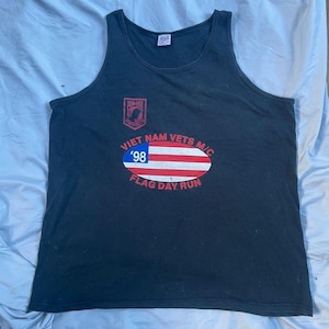 May include: A black sleeveless tank top featuring a red POW-MIA emblem on the upper left chest. The center graphic displays an oval American flag design with the text VIET NAM VETS M/C, '98, and FLAG DAY RUN printed in red and white lettering.