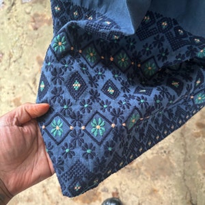 Puede incluir: Tela azul con un patr&oacute;n geom&eacute;trico de flores bordadas en tonos de rosa, verde y azul.