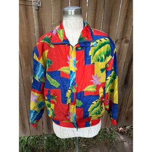 May include: A vibrant, vintage jacket with a colorful tropical print. The jacket features a red base with blue, yellow, and green geometric shapes and floral patterns. It has a zip-up front, a stand-up collar, and elastic cuffs and hem.