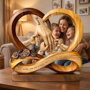 Puede incluir: Una escultura de madera con forma de símbolo de infinito y dos corazones. La escultura presenta manos talladas que se sostienen, con los nombres "Sophia", "Alex" y "David" en las muñecas. La palabra "Mommy" está en la mano. El texto dice "To the world, you are a mum, but to us, you are our whole world."