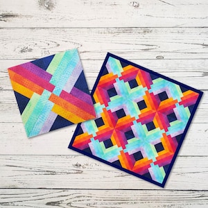 May include: Two colorful fabric squares with geometric patterns. The squares are made of a dark blue fabric with bright orange, yellow, pink, and green stripes and squares. The squares are on a white wooden surface.