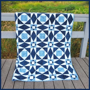 May include: A blue and white quilt with a geometric pattern. The quilt is made of fabric squares and triangles, and it has a modern design.