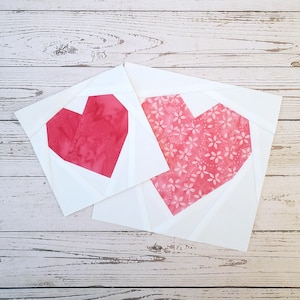 May include: Two white fabric squares with pink hearts sewn on top. The hearts are made of different fabrics, one is solid pink and the other has a white floral pattern.