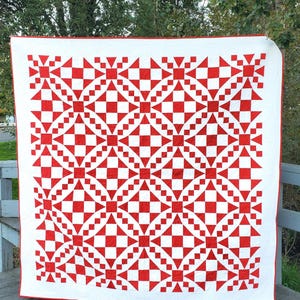 May include: A large, handmade quilt with a striking red and white geometric pattern. The design features repeating squares, triangles, and diamond shapes, creating a visually appealing and symmetrical layout. The quilt has a white background with red accents and a red border.