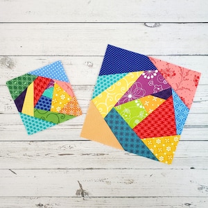 Può includere: Due blocchi di patchwork colorati a forma di spirale. Il blocco più grande è arancione, giallo, rosso, verde, blu e viola. Il blocco più piccolo è lo stesso motivo ma più piccolo. Entrambi i blocchi sono su uno sfondo di legno bianco.