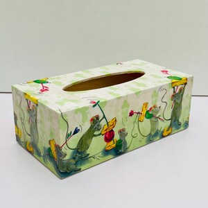 Könnte beinhalten: Ein rechteckiger Taschentuchbox-Bezug mit hellgrün-weiß kariertem Hintergrund und Illustrationen von grauen Mäusen, die gelben Käse und rote Früchte halten. Die Box hat eine ovale Öffnung an der Oberseite zur Entnahme der Tücher.
