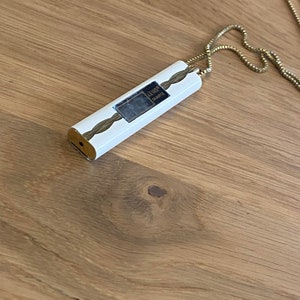 May include: A white and gold necklace with a rectangular pendant that says "LECOQ QUARTZ".