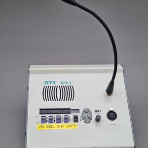 May include: A white RTS BKP-4 intercom station with a flexible black microphone. The unit has buttons for listening, talking, and call waiting. The text "VSI INSL UHF ODER" is on a yellow sticker.