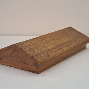 May include: A wooden box with a hinged lid. The lid is carved with intricate patterns and the box is made of light brown wood.