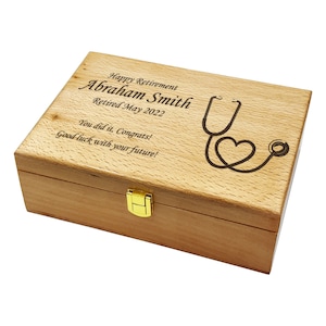 May include: A wooden box with a gold latch. The lid is engraved with the text "Happy Retirement Abraham Smith Retired May 2022 You did it, Congrats! Good luck with your future!" and a stethoscope with a heart.