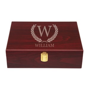 May include: A mahogany wood box with a gold latch. The top of the box is engraved with a laurel wreath and the letter "W" inside the wreath. The name "WILLIAM" is engraved below the wreath.
