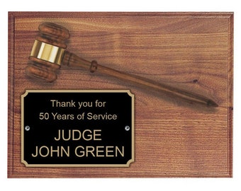 May include: A wooden plaque with a gavel and a black nameplate. The nameplate reads "Thank you for 50 Years of Service JUDGE JOHN GREEN". The gavel is brown with a gold band. The plaque has a wood grain finish.