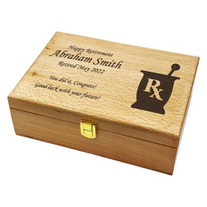 May include: A wooden box with a gold latch. The lid is engraved with the text "Happy Retirement Abraham Smith Retired May 2022 You did it, Congrats! Good luck with your future!" and a mortar and pestle with the letter "R" inside.