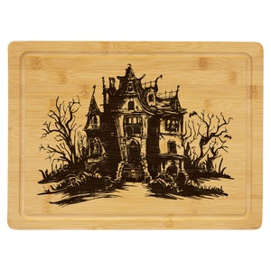 May include: A brown bamboo chopping board with a black and white illustration of a spooky haunted house with trees on either side.