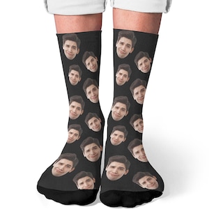 May include: Black socks featuring a repeating pattern of a person's face. The faces are smiling and have dark hair. The socks are worn on a person's legs, with the feet and ankles visible.
