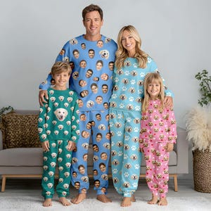 May include: A family of four wearing matching pajamas. The adults wear blue pajamas with faces printed on them. The children wear green and pink pajamas with dog faces and paw prints. The pajamas are made of a soft material.