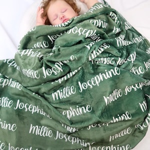 May include: A dark green blanket with the name "Millie Josephine" printed in white script. The blanket is draped over a sleeping baby. The blanket appears soft and plush.