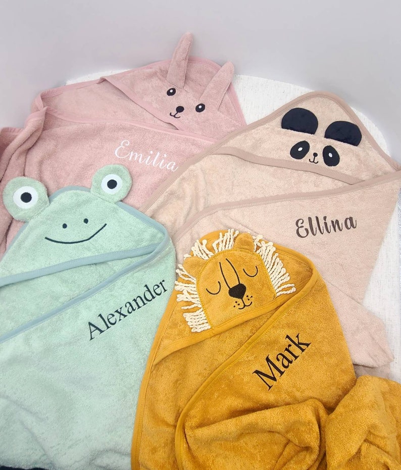 K&ouml;nnte beinhalten: Vier Kapuzenhandt&uuml;cher f&uuml;r Babys in Pastellfarben: Rosa, Beige, Hellgr&uuml;n und Gelb. Jedes Handtuch hat ein Tiergesicht auf der Kapuze: ein Hase, ein Panda, ein Frosch und ein L&ouml;we. Namen sind aufgestickt: Emilia, Ellina, Alexander und Mark.