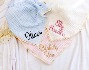 May include: Three personalized baby bibs in light blue, white, and pink, each with a name embroidered in a contrasting color. The bibs have a ruffled lace trim.