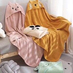 K&ouml;nnte beinhalten: Eine Auswahl an Baby-Handt&uuml;chern mit Kapuze in verschiedenen Farben und Tiermotiven. Die Handt&uuml;cher zeigen einen rosa Hasen, einen goldenen L&ouml;wen, einen beigen Panda und einen hellgr&uuml;nen Frosch. Die Handt&uuml;cher sind weich und flauschig, ideal f&uuml;r das Baden.