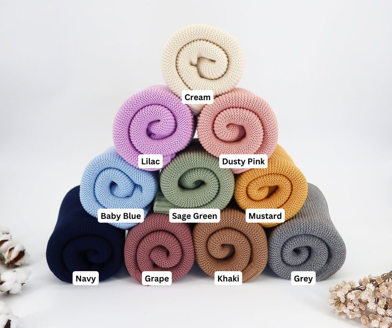 May include: A collection of rolled knit blankets in various colors, including cream, lilac, dusty pink, baby blue, sage green, mustard, navy, grape, khaki, and grey. Each blanket is labeled with its color name.