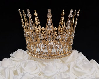 May include: A gold crown with clear rhinestones, sitting on a bed of white roses.