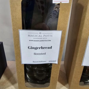 May include: A brown cardboard box with a rectangular cutout window containing a glass reed diffuser. The label reads Magical Potts Handmade Gifts, www.magicalpotts.com, Gingerbread Scented, Reed Diffuser 100ml. A small white price tag reads 10.00.