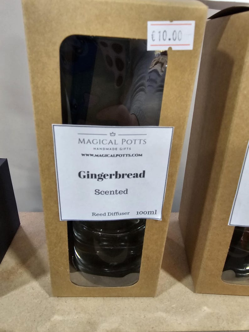 May include: A brown cardboard box with a rectangular cutout window containing a glass reed diffuser. The label reads Magical Potts Handmade Gifts, www.magicalpotts.com, Gingerbread Scented, Reed Diffuser 100ml. A small white price tag reads 10.00.