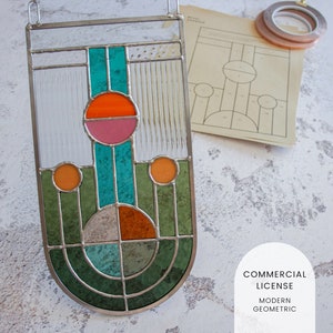 May include: A stained glass window panel with a modern geometric design. The panel features a teal, orange, and pink circle design with green and gray accents. The panel is hung on a white wall with a piece of paper and tape in the background. The text "COMMERCIAL LICENSE MODERN GEOMETRIC" is visible in the bottom right corner of the image.