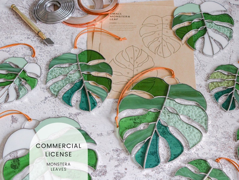Peut inclure: Un ensemble de feuilles de monstera en verre teint&eacute; dans diff&eacute;rentes nuances de vert, de blanc et de vert clair. Les feuilles sont suspendues &agrave; des cordons orange et ont un contour argent&eacute;. L'image comprend &eacute;galement une feuille de papier avec un motif pour r&eacute;aliser les feuilles et un rouleau de ruban adh&eacute;sif en cuivre.